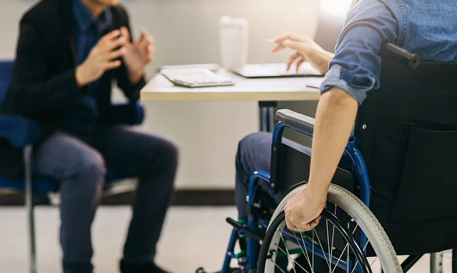 Person in wheelchair talking with someone at a table, highlighting inclusivity